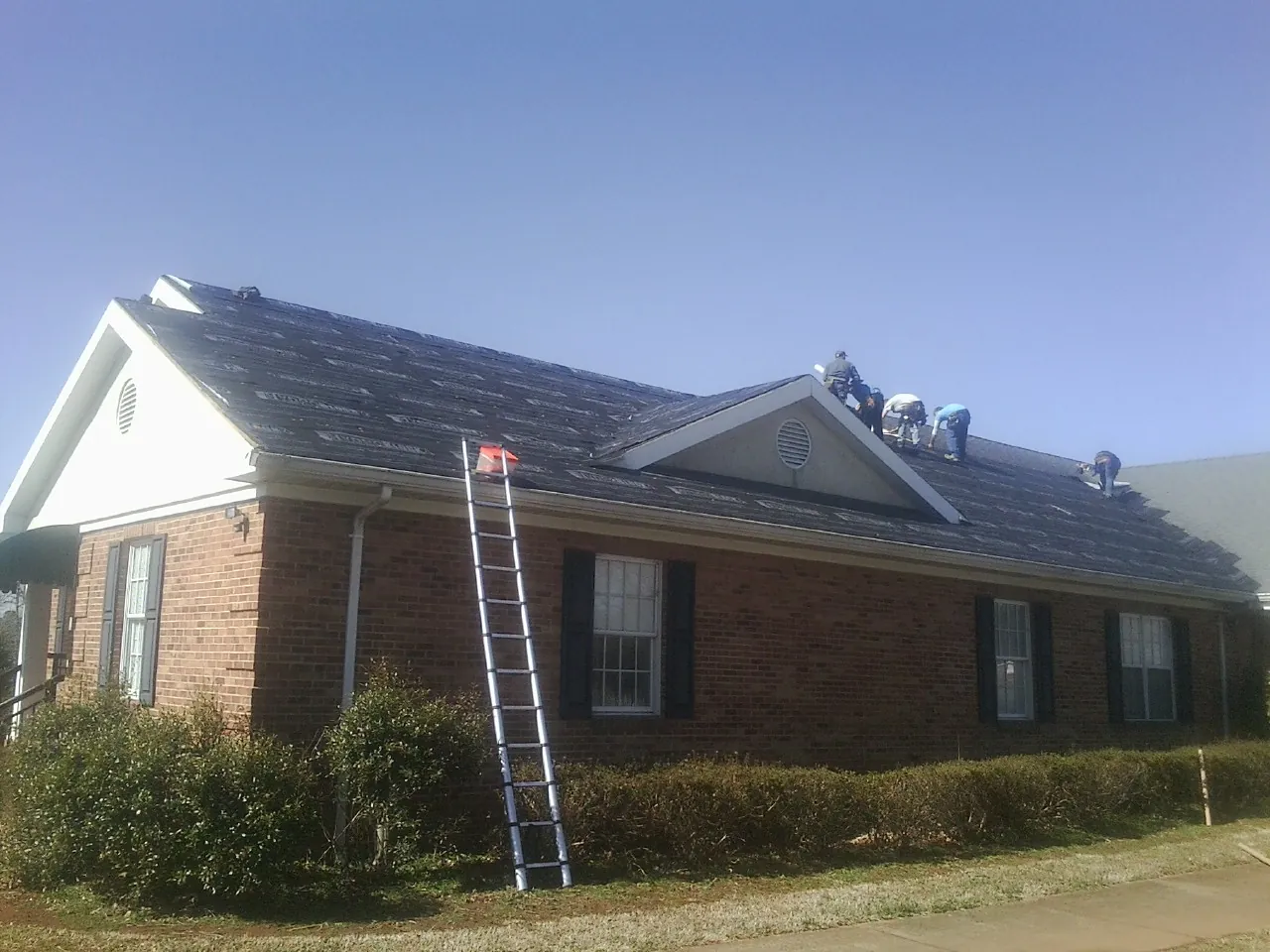 Crew tearing shingles off a brick ranch roof with a ladder set — Emergency Roof Repair work by our crew in Hamburg